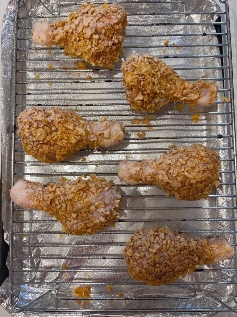 Breaded drumsticks arranged on a rack, sprayed with canola oil