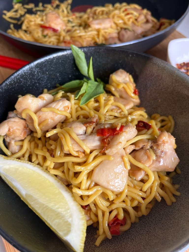 Chilli chicken Hokkien stir-fry served in a bowl with lemon and chilli flakes