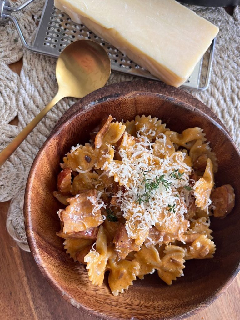 Creamy chorizo and bacon pasta served in a rustic wooden bowl, placed next to a block of parmesan cheese and a grater