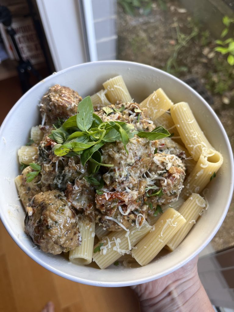 Creamy pork meatballs served over rigatoni in a white bowl, held by a female hand