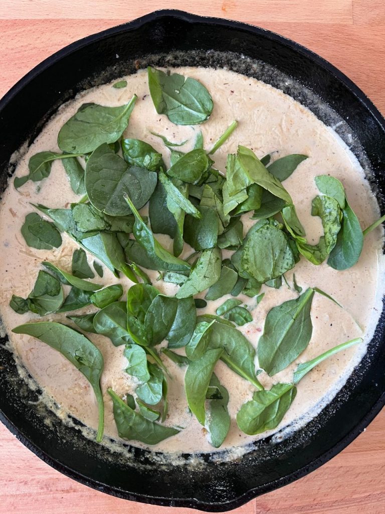 Fresh baby spinach leaves scattered over creamy sauce in a skillet, ready to wilt into the mixture