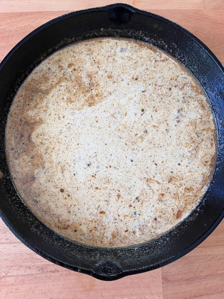 Heavy cream being stirred into the skillet, creating a smooth sauce, gently simmering with seasonings.