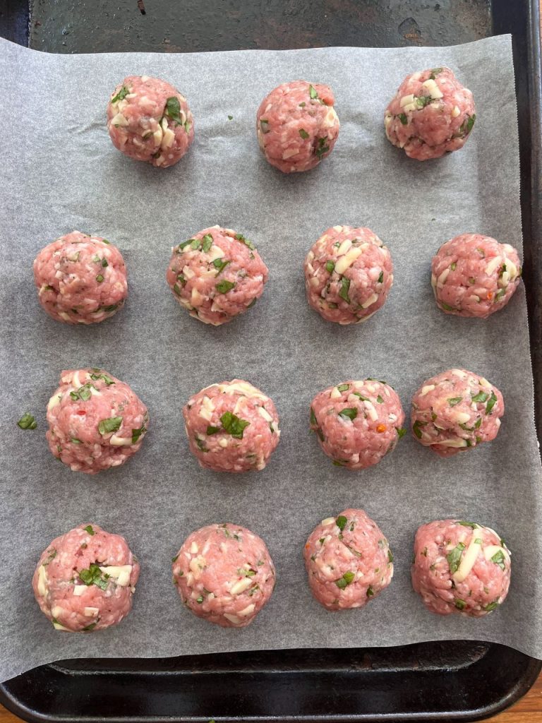 Raw pork meatballs mixed with mozzarella and spices, arranged on a tray