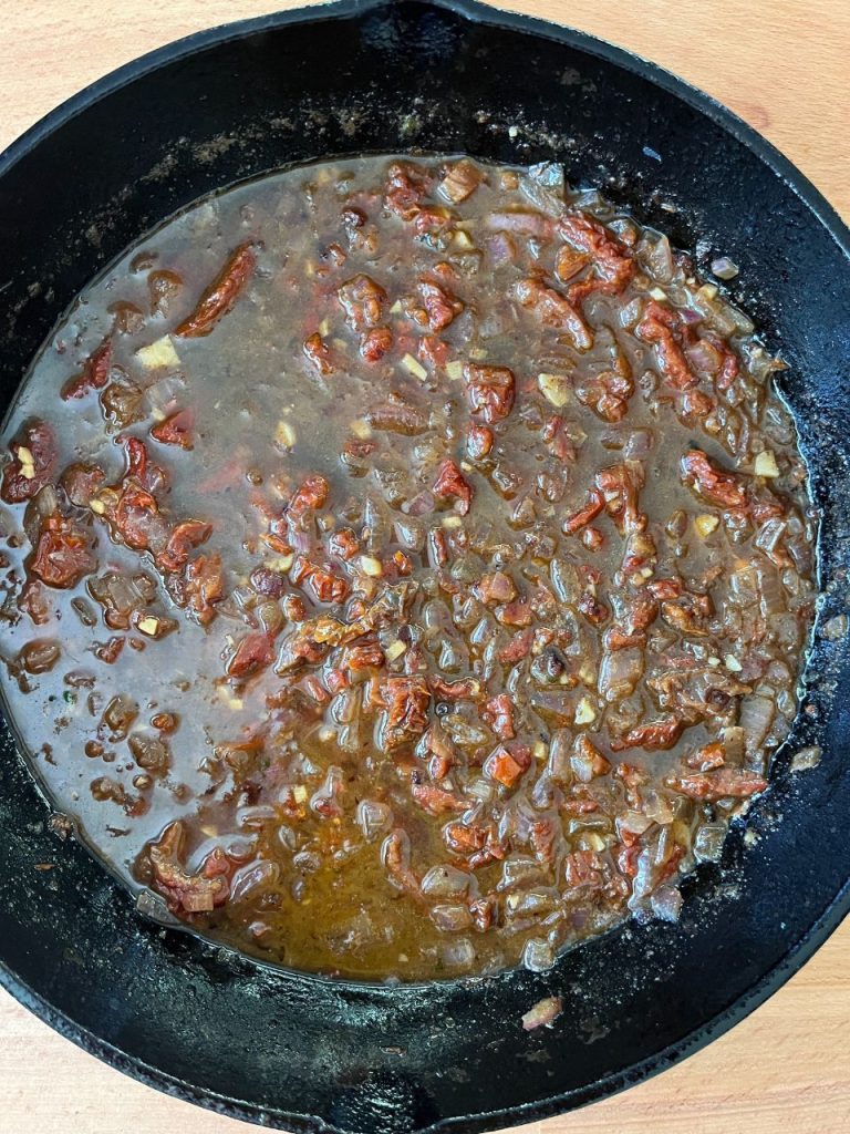 Sun-dried tomatoes and onions sautéing in a skillet with garlic, butter and white wine