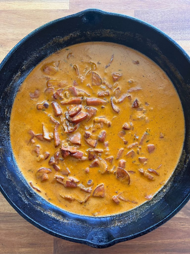 Thickened creamy sauce simmering with chorizo and bacon in a frying pan