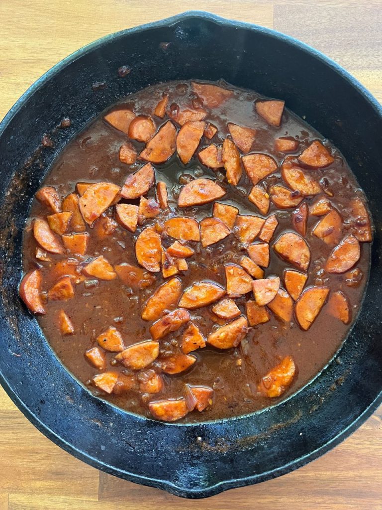 Tomato paste, chicken stock, and thyme mixed in a pan with chorizo and bacon