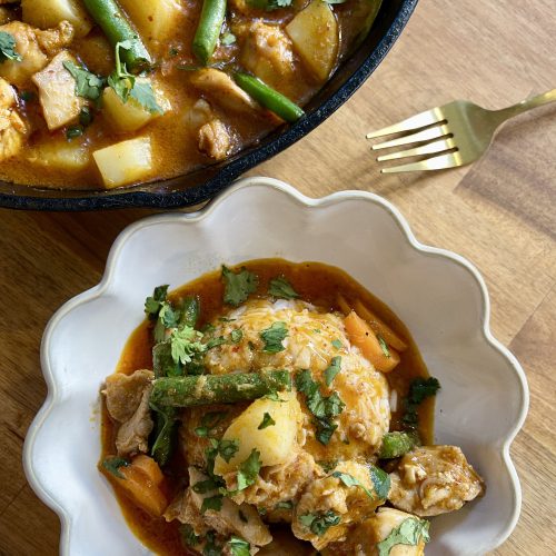 Overhead shot of Thai red curry with chicken in a white bowl, with vibrant vegetables and creamy sauce
