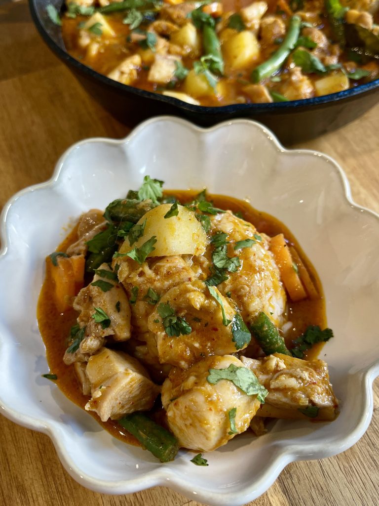 Thai red curry with chicken served on a bed of rice in a white bowl, garnished with Thai basil and coriander
