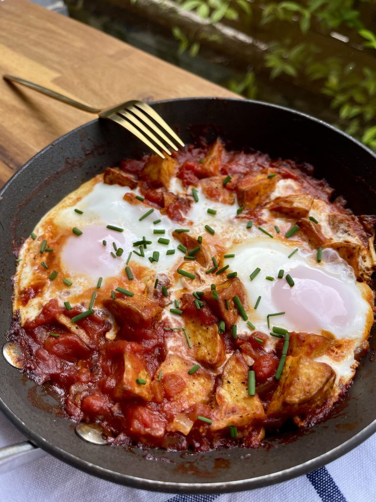 Close-up of a perfectly cooked egg with a runny yolk nestled in the tomato and potato mixture