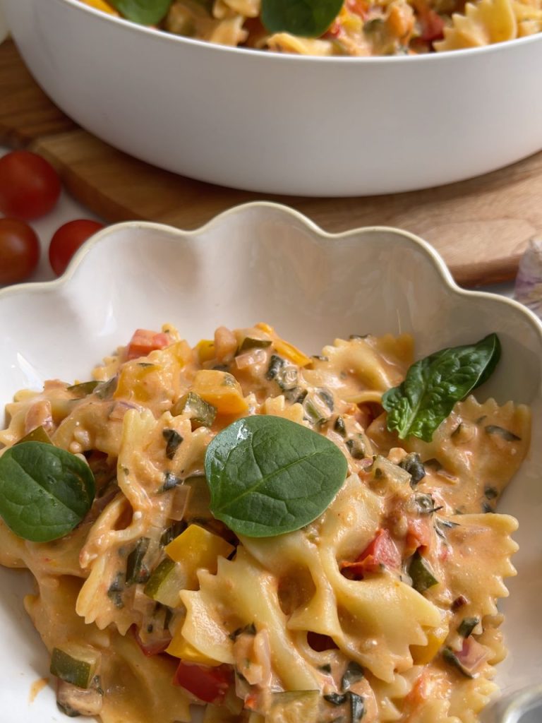 Close-up of pasta coated in a rich, creamy vegetable sauce, with fresh basil and parmesan sprinkled on top