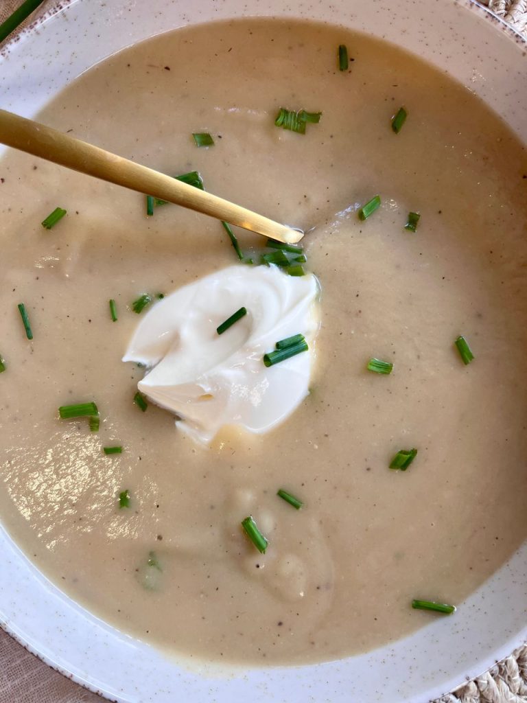 Creamy potato and leek soup served in a white bowl, topped with crème fraîche and chopped chives