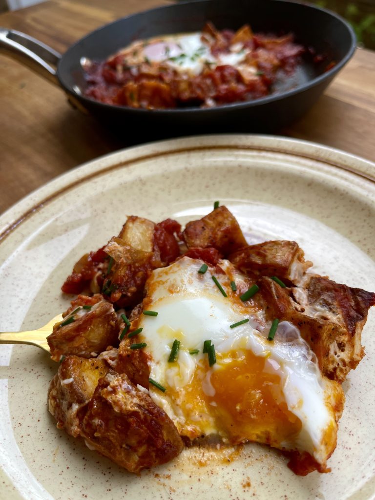 Egg and potato skillet plated on a plate with the frying pan in the background