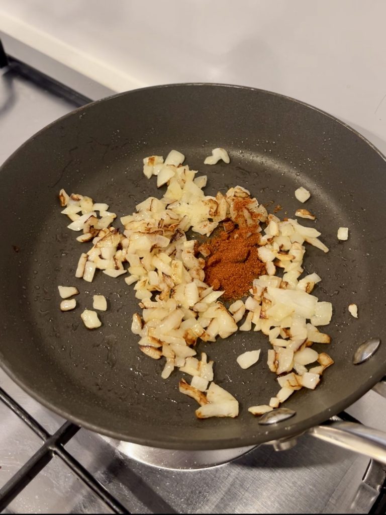 Onion and garlic sautéing in a small frying pan, turning soft and translucent