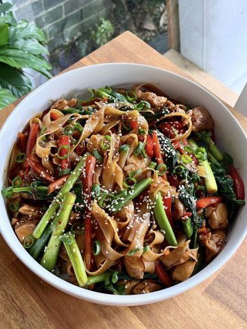 Overhead shot of drunken noodles in a white scallop-edge bowl, showcasing glossy noodles and fresh veggies