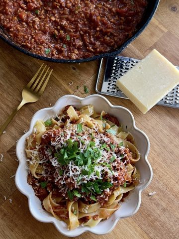 Overhead shot of pork and chorizo ragu in a white scalloped bowl, with a brass fork resting on the side