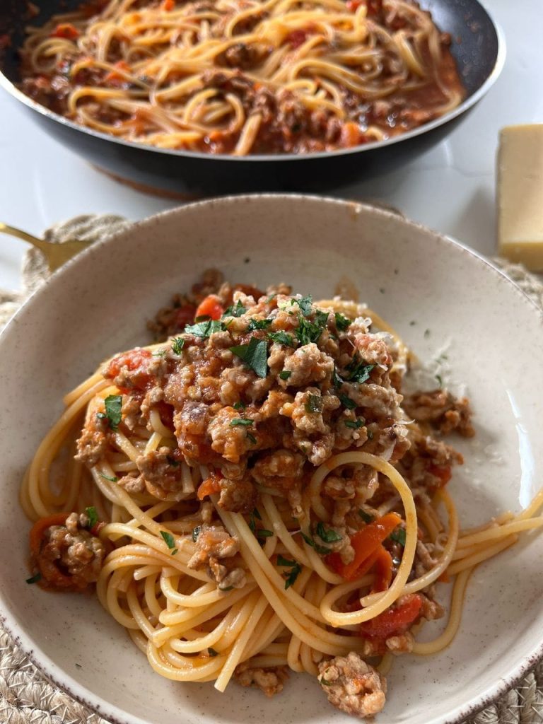 Overhead shot of pork sugo spaghetti in a bowl, garnished with parmesan shavings