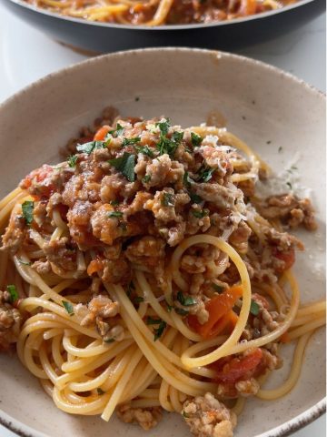 Pork and chilli sugo spaghetti served in a bowl, topped with grated parmesan and fresh parsley