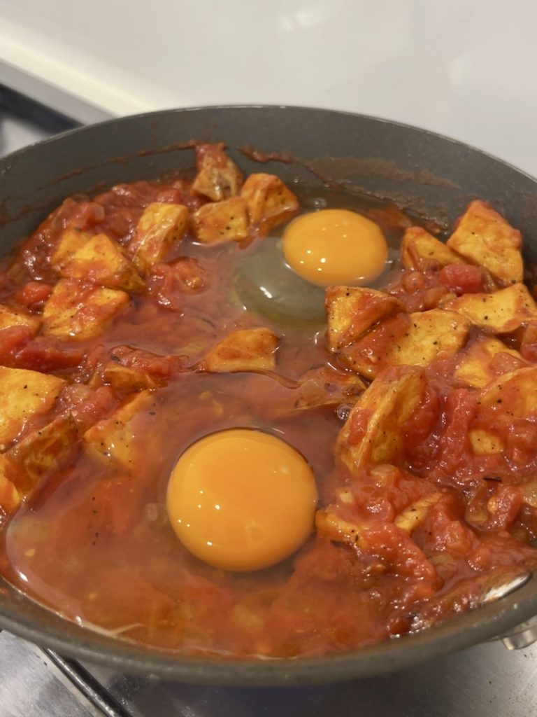 Two wells made in the tomato and potato mixture, eggs cracked in
