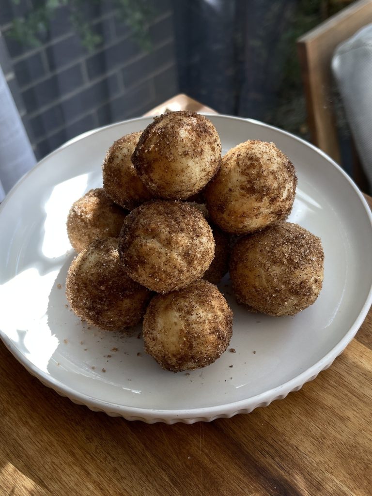 Cinnamon donut bites stacked on a white plate, golden and coated in cinnamon sugar
