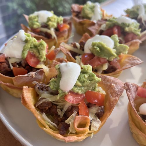 Close-up of a single taco cup showing layers of beef, melted cheese, fresh lettuce, and creamy toppings