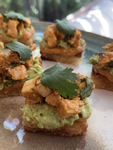 Close-up of crispy rice squares layered with chipotle chicken, drizzled with mayo and garnished with herbs