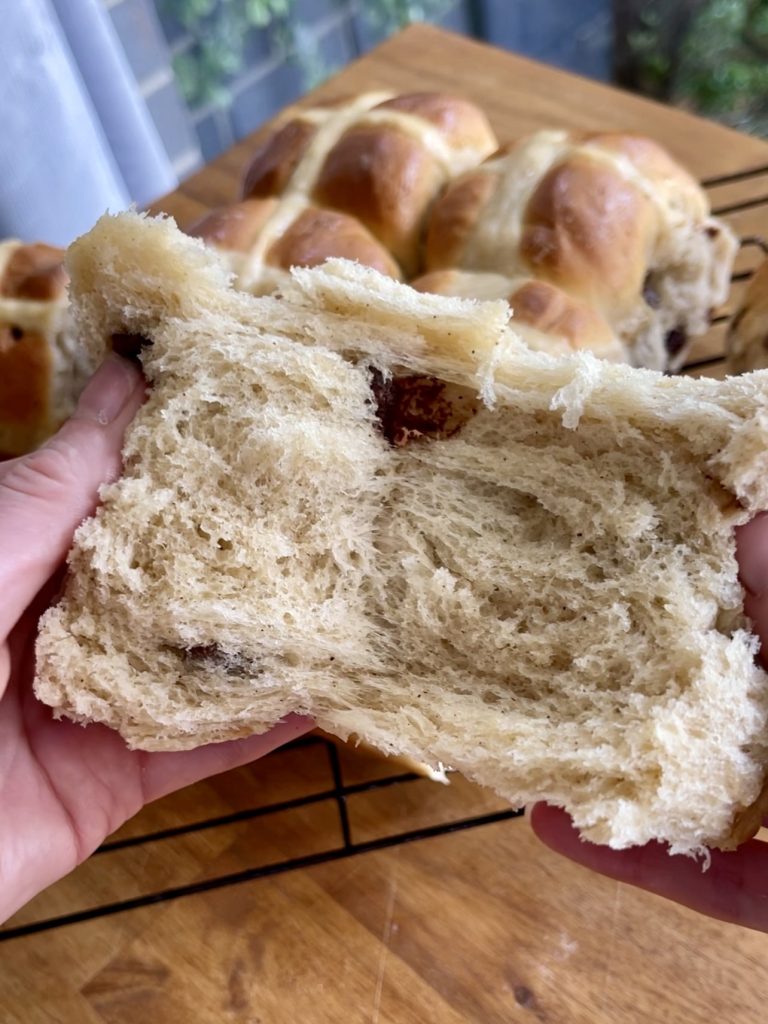 Close-up of hot cross bun torn in half, revealing soft, fluffy interior with melted chocolate chips