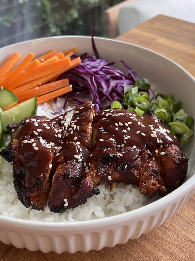 Close-up of juicy gochujang chicken on rice, drizzled with spicy dressing and garnished with sesame seeds