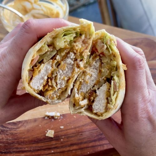 Crispy chicken cornflake wrap cut in half, filled with golden chicken, fresh lettuce, tomato, cheese, and bacon
