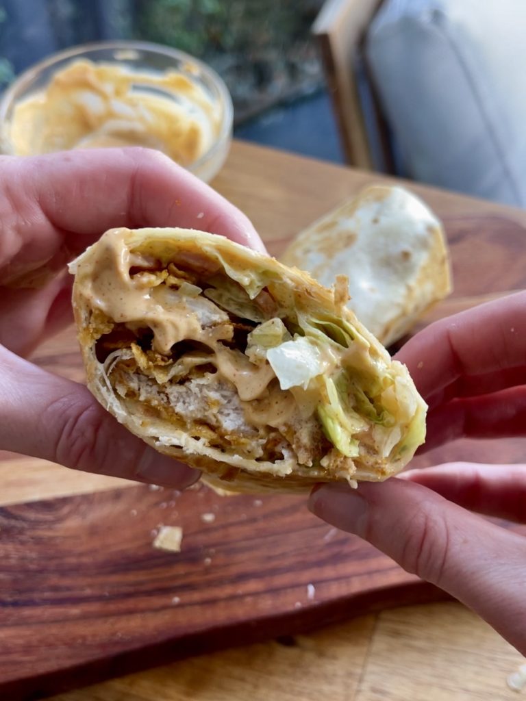 Crispy chicken cornflake wrap sliced in half, extra chipotle mayo drizzled on top