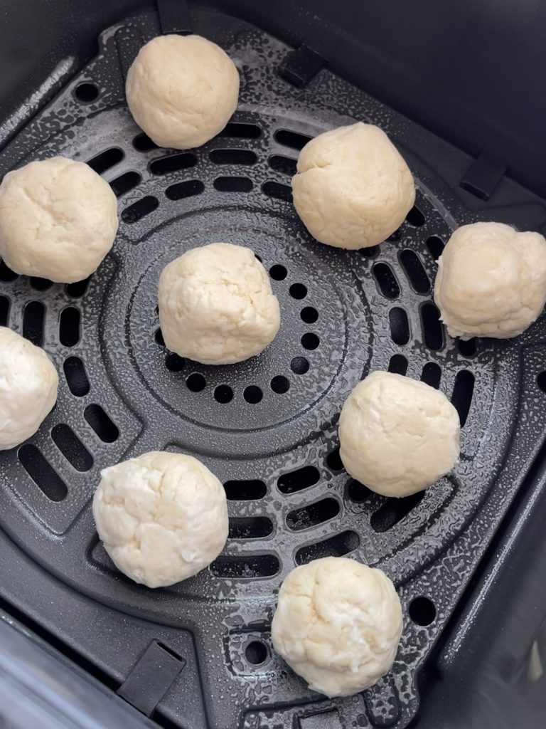 Dough balls placed in an air fryer basket, lightly sprayed with oil and baking at 180°C