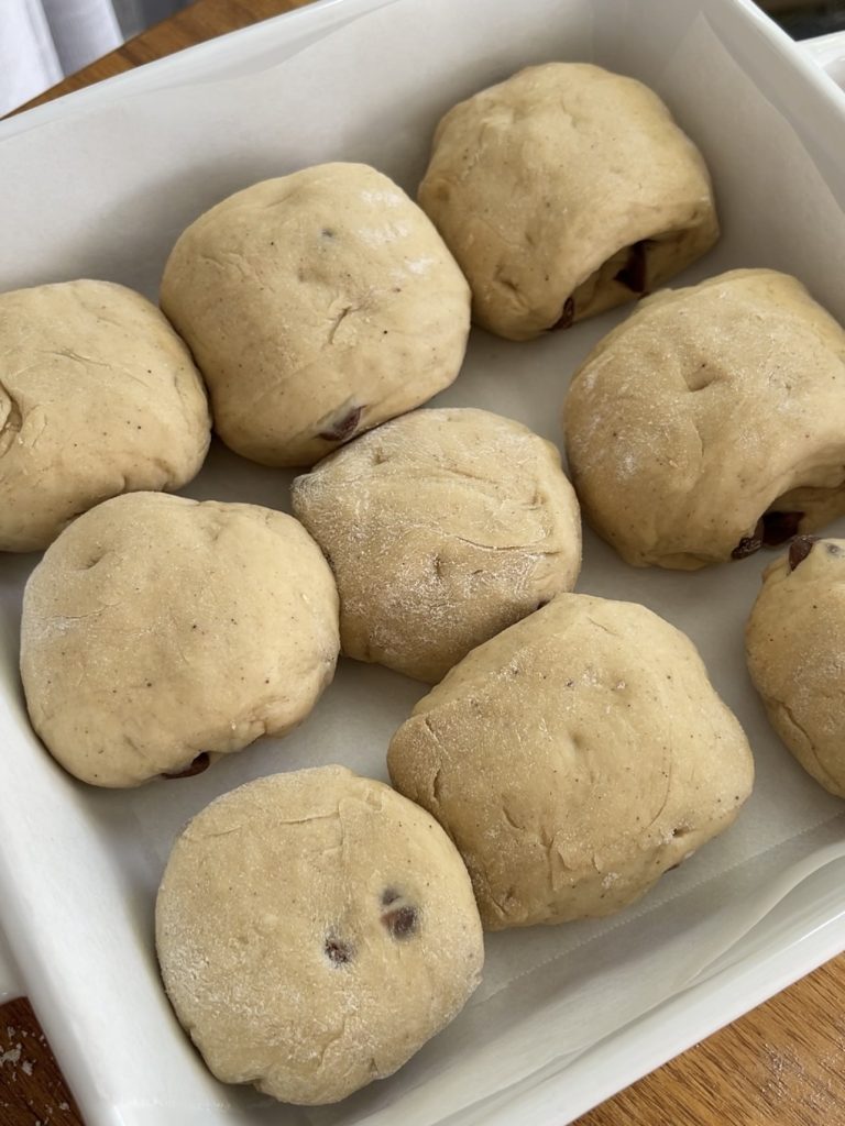 Dough log divided into 9 equal pieces, shaped into round buns and arranged on a lined baking tray
