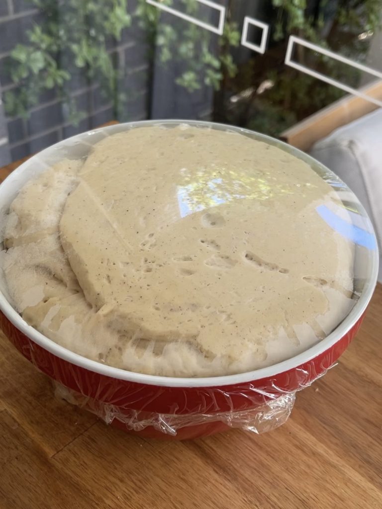 Dough resting in a greased bowl covered with cling wrap, placed in a warm spot to rise