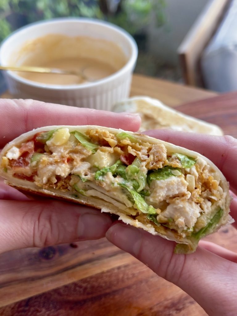 Hand holding one half of the chopped chicken crunch wrap, showing its crunchy coating and colourful filling