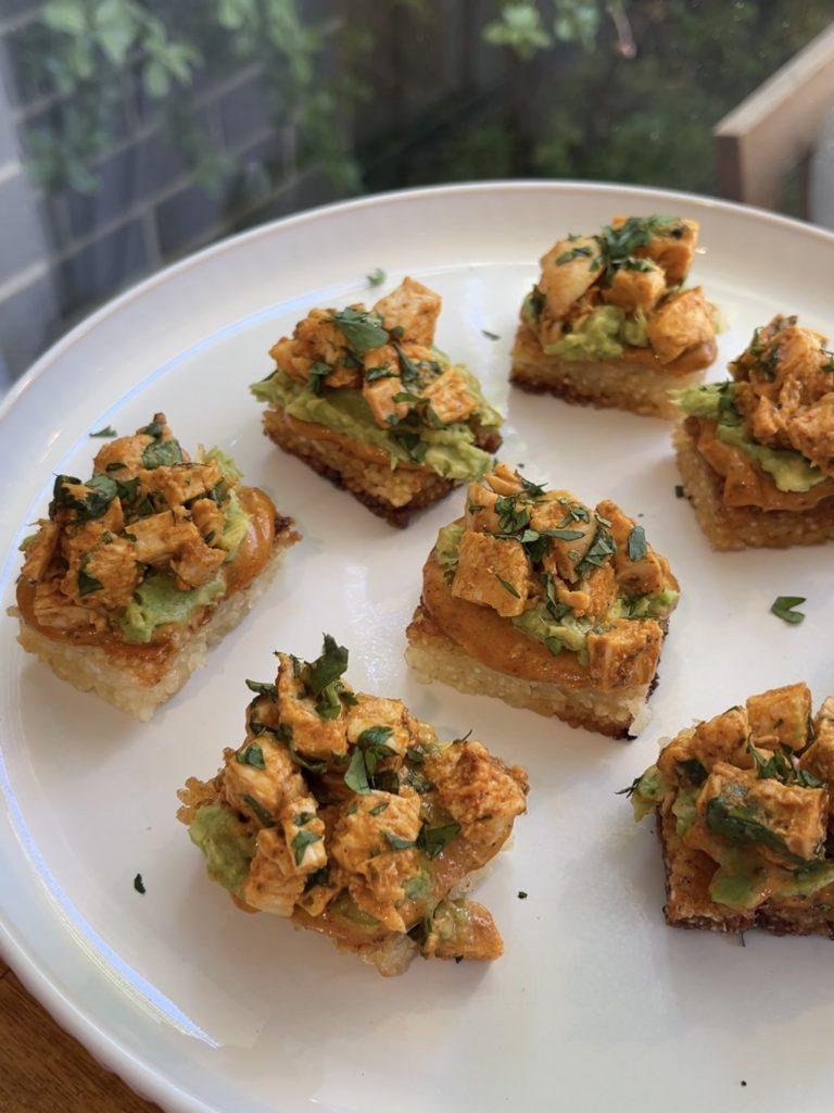 Overhead shot of chipotle chicken rice bites arranged on a white platter, topped with vibrant avocado and coriander