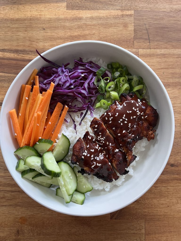 Overhead shot of gochujang chicken bowl with vibrant toppings—carrot, cucumber, cabbage, and spring onion