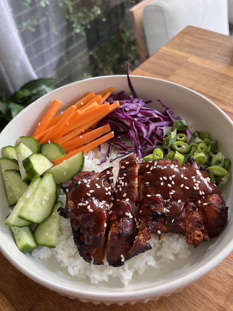 Sliced gochujang chicken resting on fluffy white rice, surrounded by colourful salad ingredients in a bowl