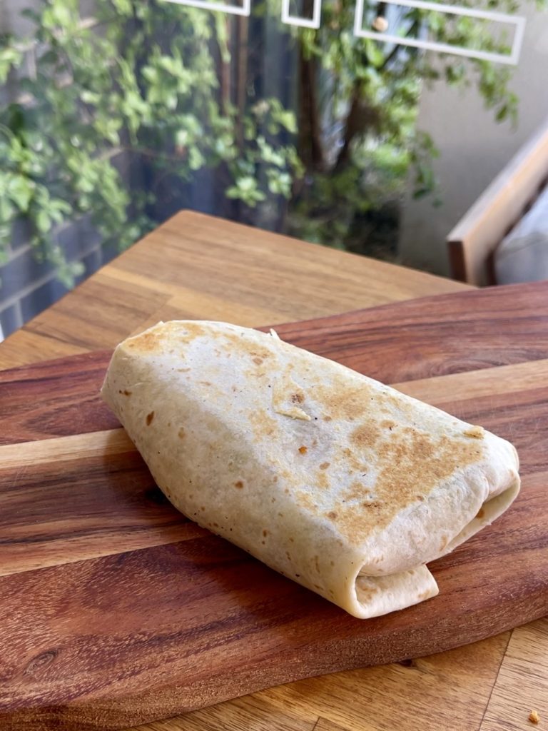 Toasted golden crunch wrap resting the a chopping board, ready to be sliced