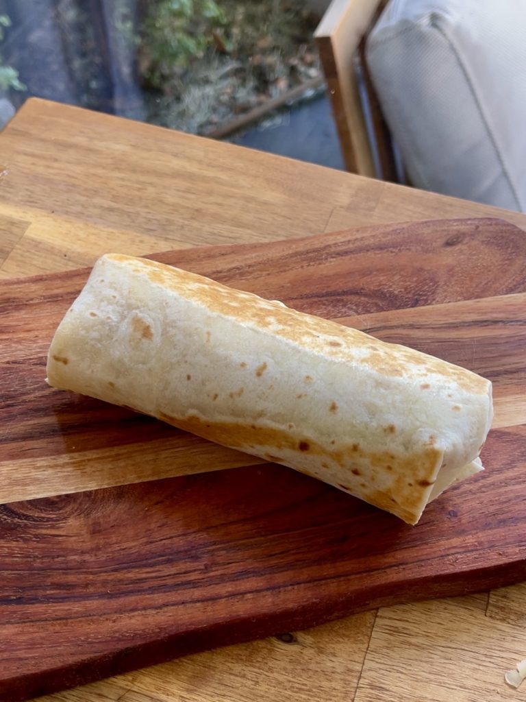 Tortilla wrapped into a burrito shape, toasted golden brown resting on a chopping board