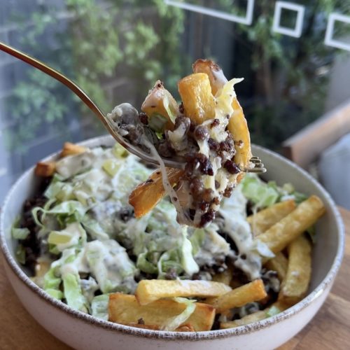 A fork lifting a bite of loaded fries, showing all the layers—cheese, beef, pickles, and lettuce