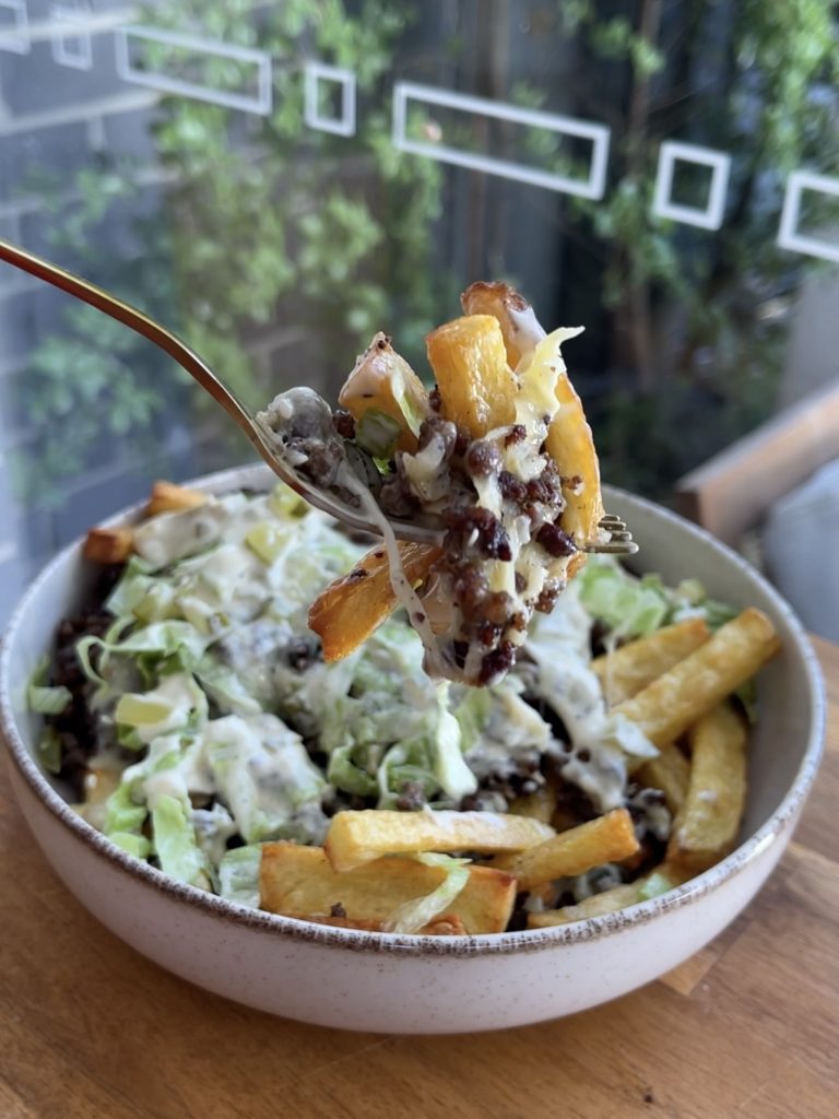 A fork lifting a bite of loaded fries, showing all the layers—cheese, beef, pickles, and lettuce