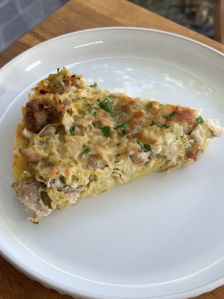 A slice of chicken and leek tart served on a plate, showing the creamy filling and golden potato crust
