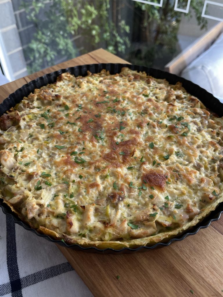 Baked chicken and leek tart fresh out of the oven, cheese bubbling on top and flecks of green herbs scattered across