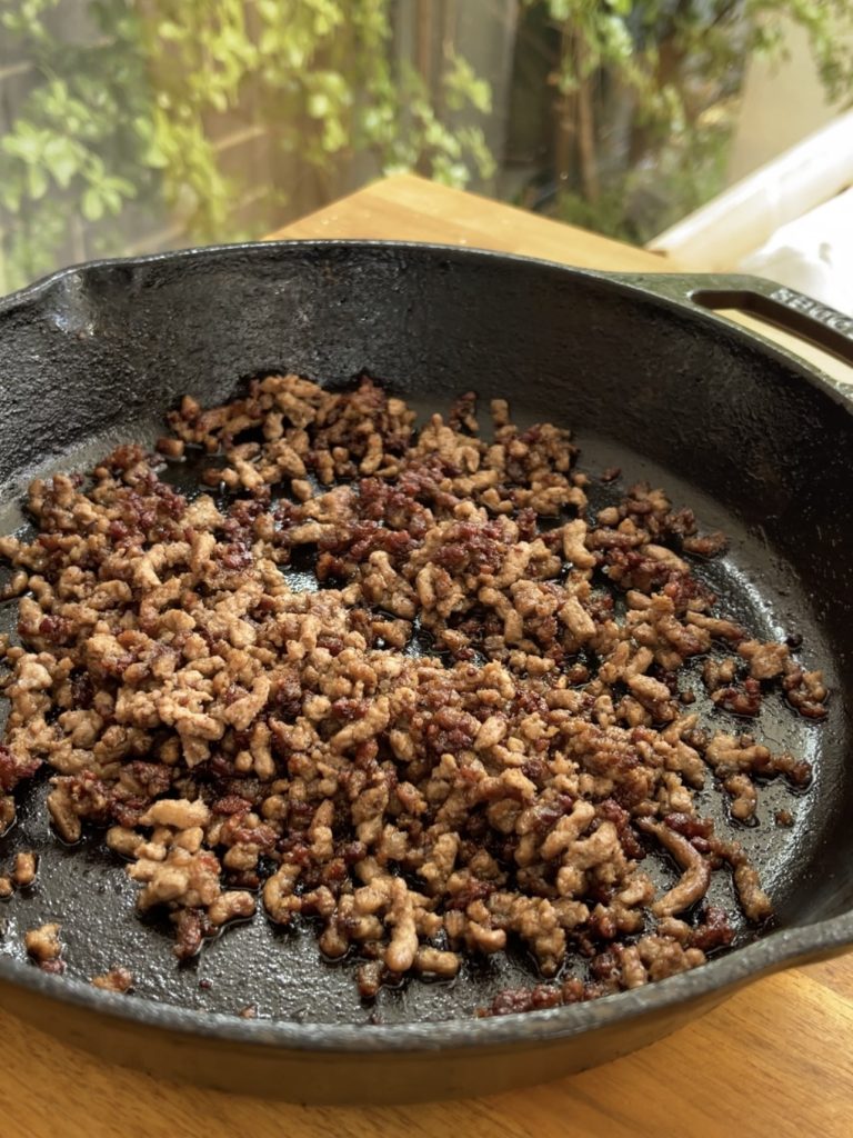 Beef mince cooking in a frying pan with oil, browning evenly and seasoned with salt and pepper