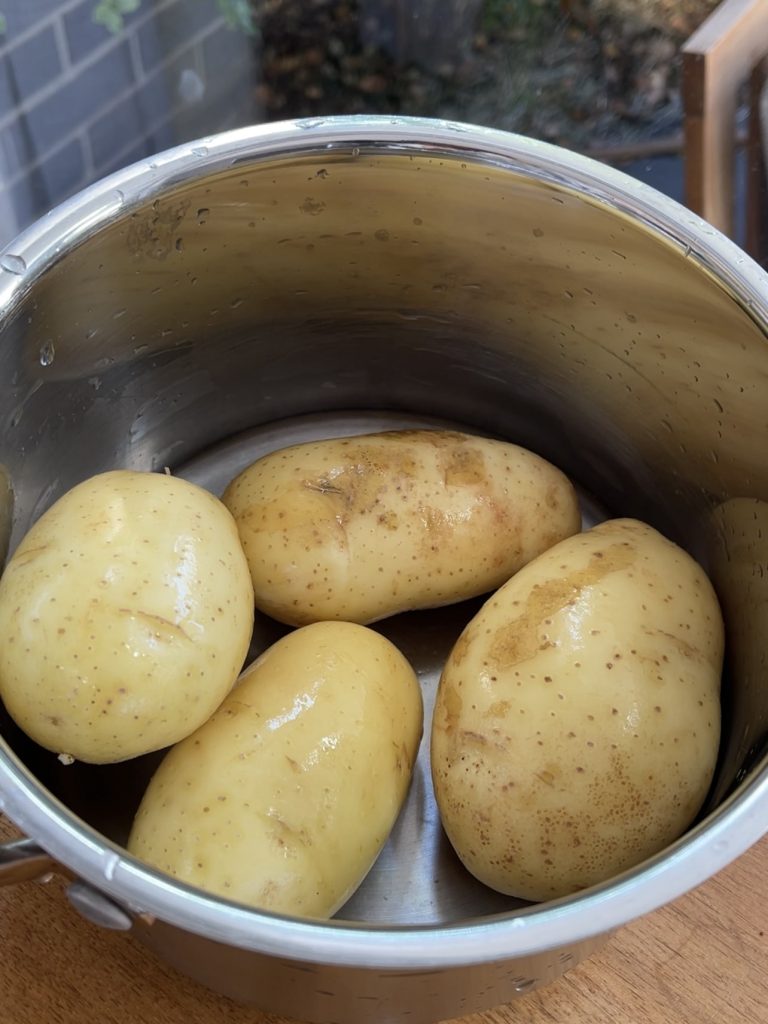 Four washed potatoes in a large pot waiting for water to be poured in
