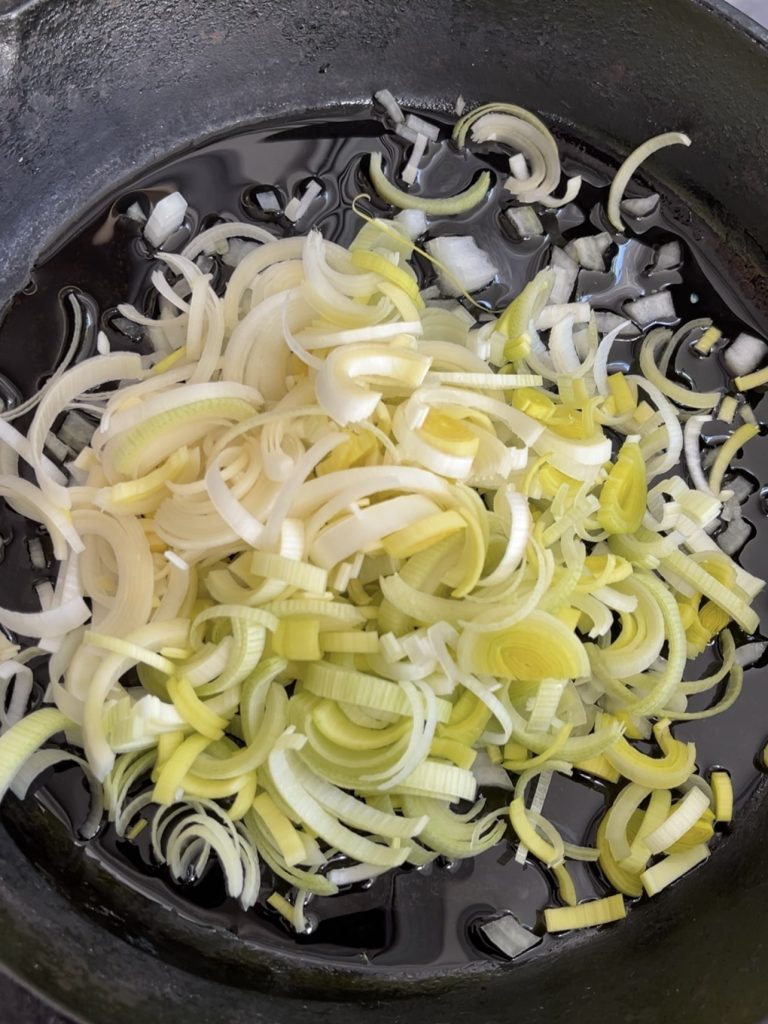 Onion, spring onion, and sliced leek sautéing in a frying pan with olive oil until softened and fragrant