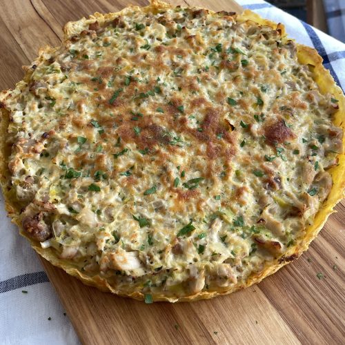 Overhead shot of the tart with a potato crust, golden cheese topping, and green herb garnish