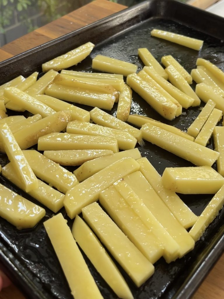 Raw potato slices tossed with olive oil and salt, spread onto a baking tray ready for roasting