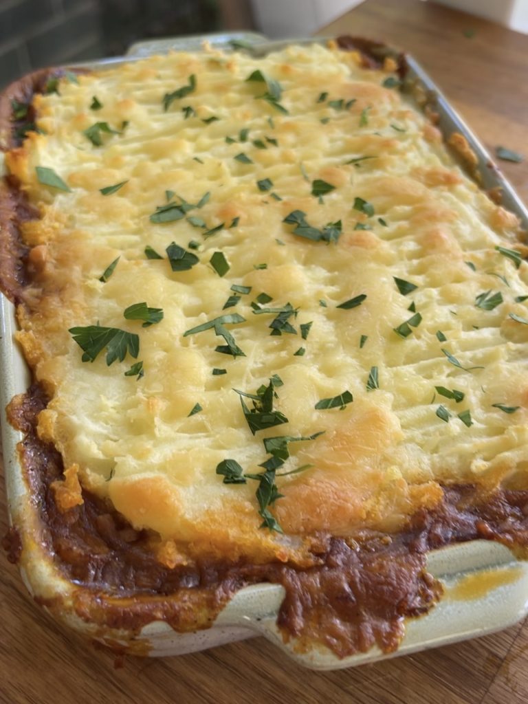 Shepherd’s pie resting on a wooden board, freshly baked with parmesan topping and crispy browned edges