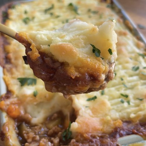 Spoonful of shepherd’s pie lifted from the baking dish, revealing the savoury meat and veggie base beneath fluffy mash