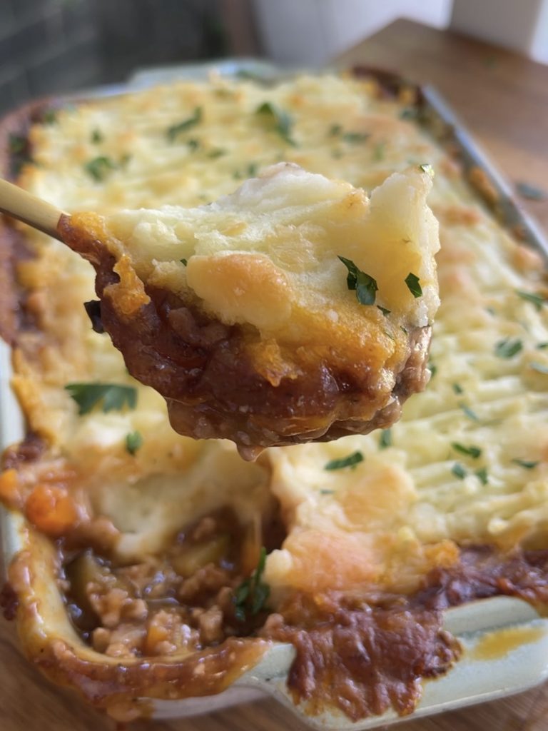 Spoonful of shepherd’s pie lifted from the baking dish, revealing the savoury meat and veggie base beneath fluffy mash